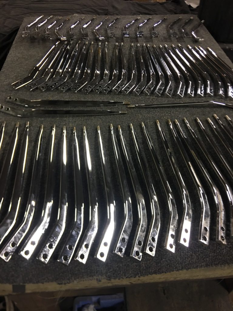 Dozens of chrome-plated shifter arms laid out in rows after polishing, reflecting light with a mirror finish.
