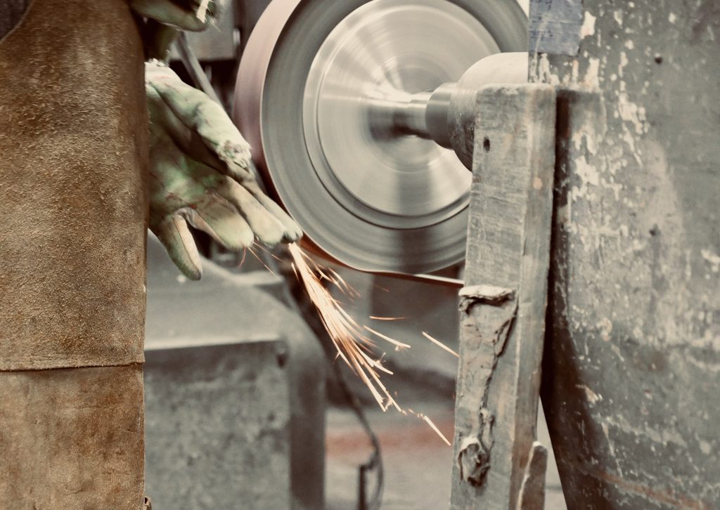 Metal polishing with a hand sander with a polishing disk. Toned image. Hand grinder workflow creation stainless pipe. from the side view