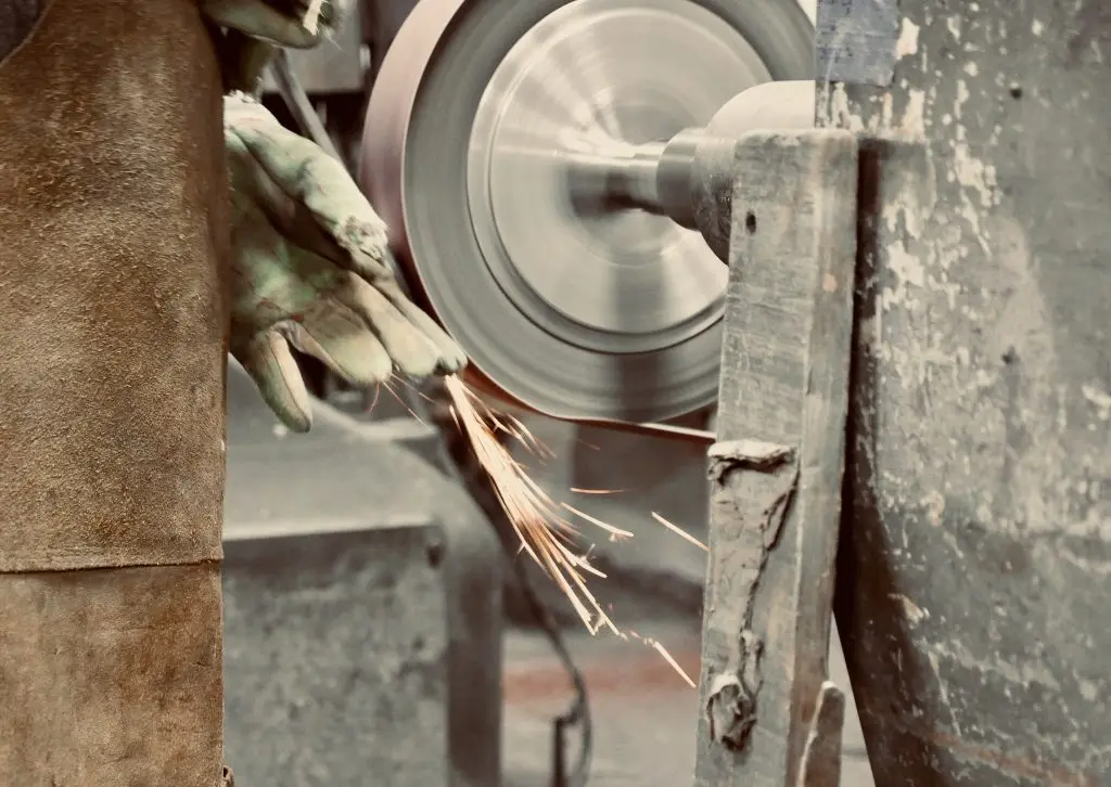 Metal polishing with a hand sander with a polishing disk. Toned image. Hand grinder workflow creation stainless pipe. from the side view